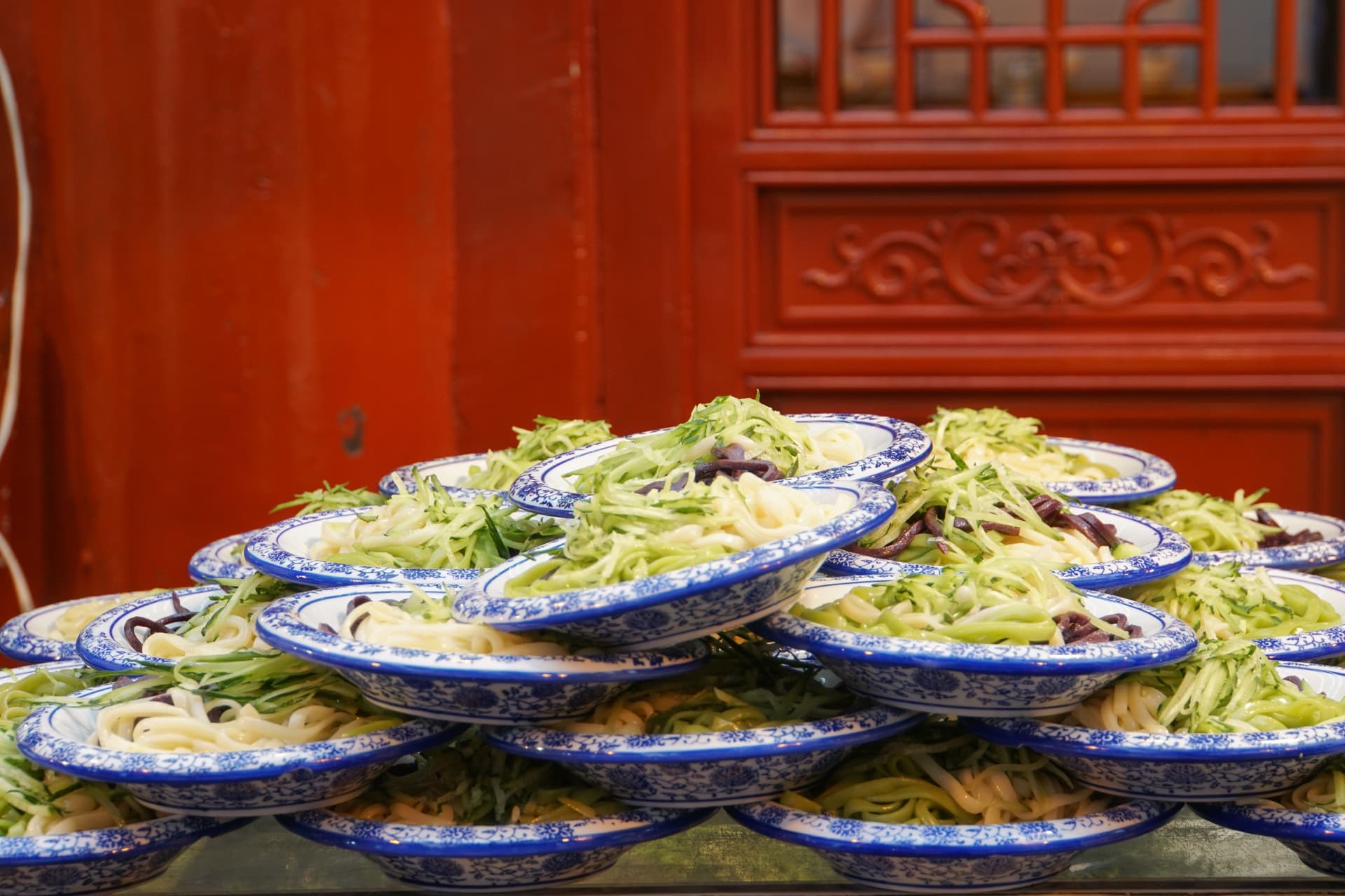 Stacks of blue and white bowls filled with chilled noodles topped with shredded cucumber at a street food stall in China.