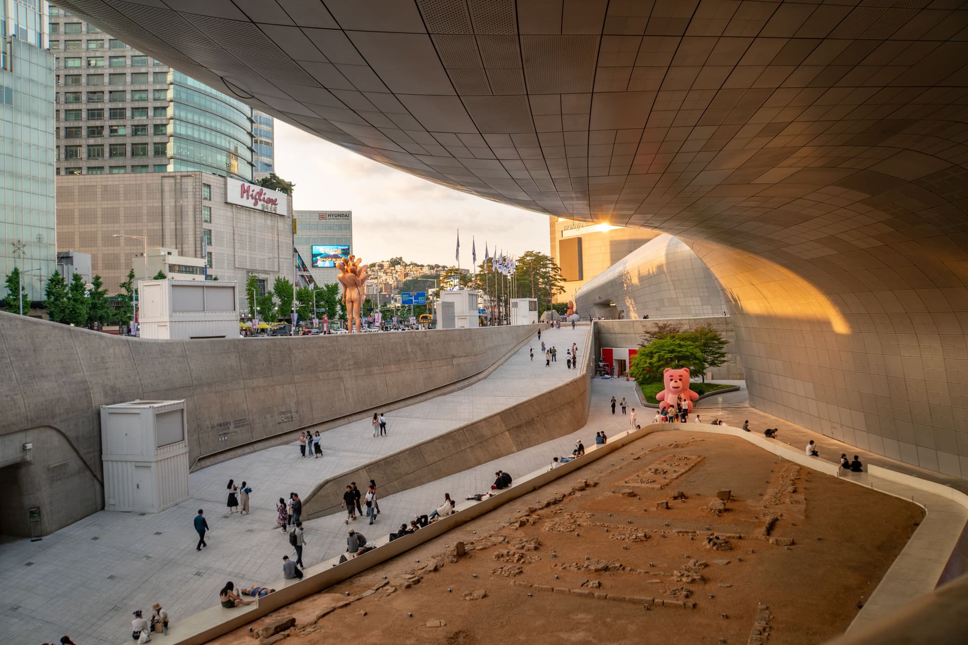 Dongdaemun Design Plaza in Seoul, South Korea, with sweeping futuristic architecture, a public walkway, and visitors at sunset.