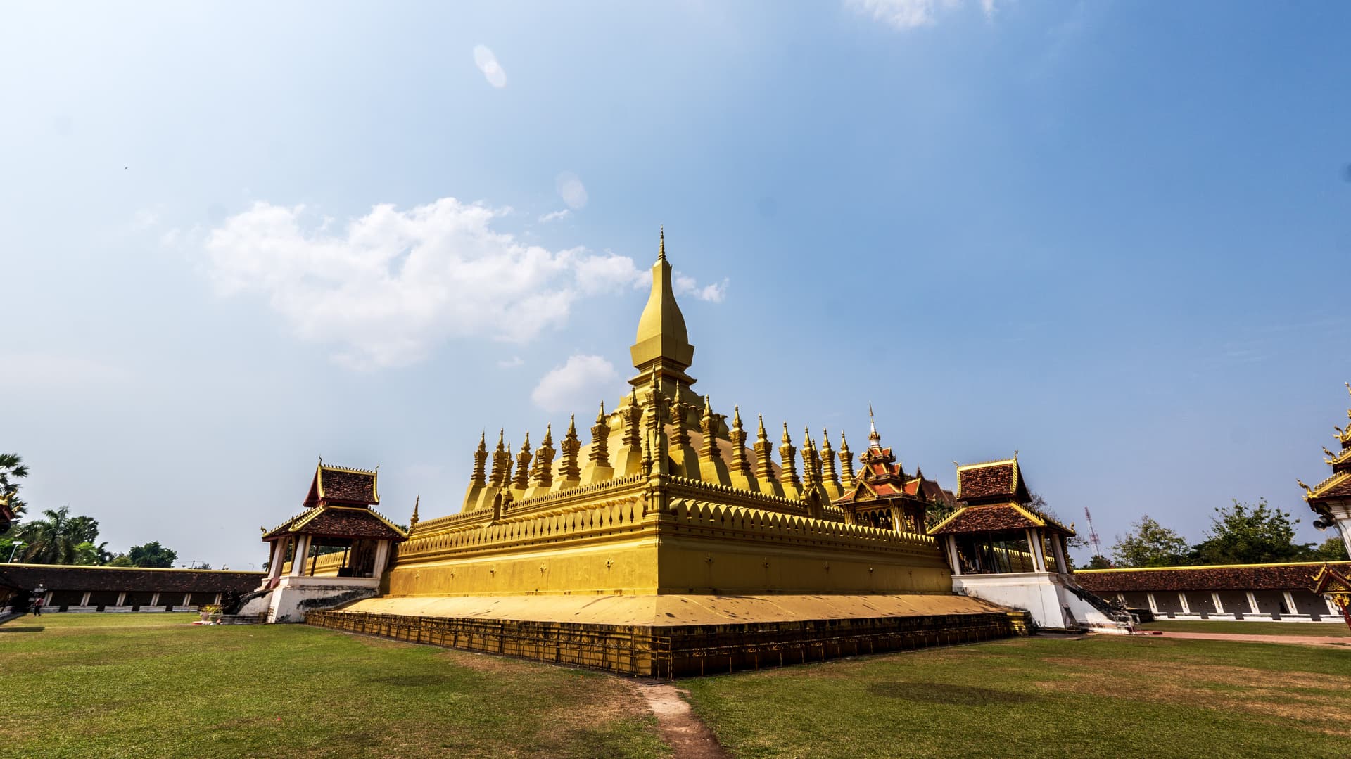 Pha That Luang golden stupa in Vientiane, Laos, viewed from the front under a clear blue sky with surrounding temple buildings.