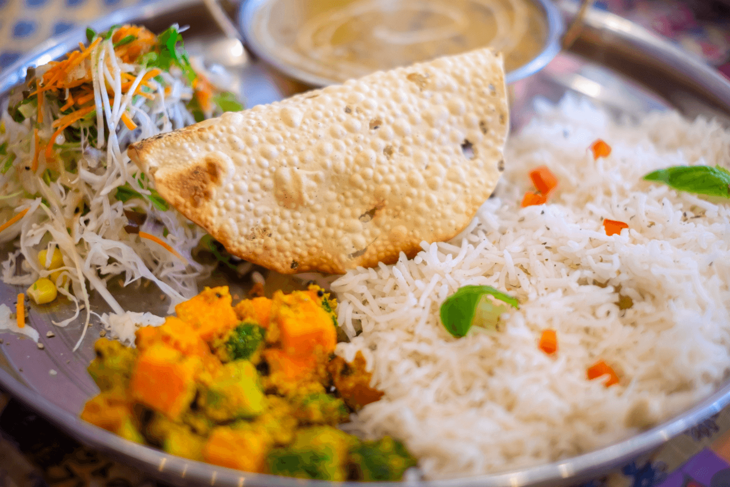 Dal bhat set with steamed rice, lentil soup, mixed vegetable curry, fresh salad, and a crispy papad on a metal plate.